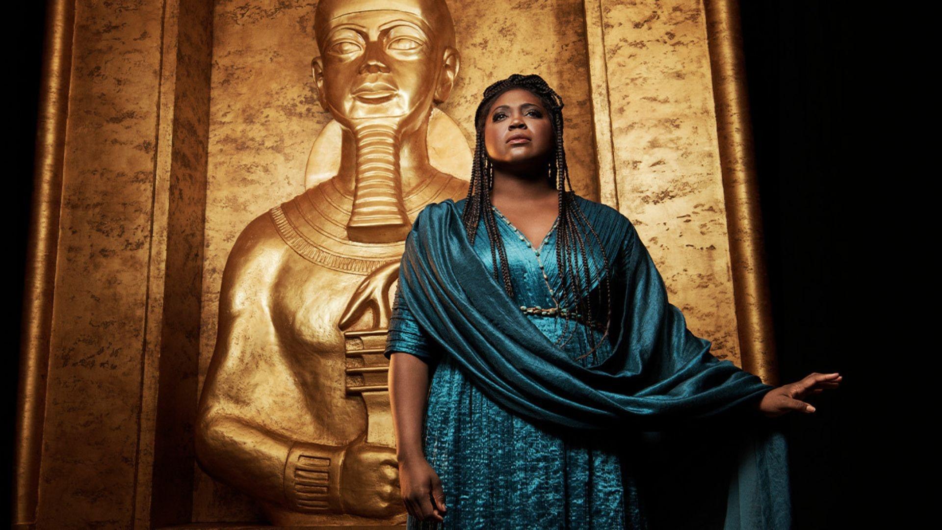 "Aida" standing in front of a large, gold, ancient egypt-like tomb