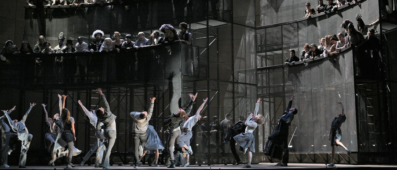 Scene from Orfeo ed Eurdice where there are dancers on the stage with other cast members on risers behind them, looking down and watching