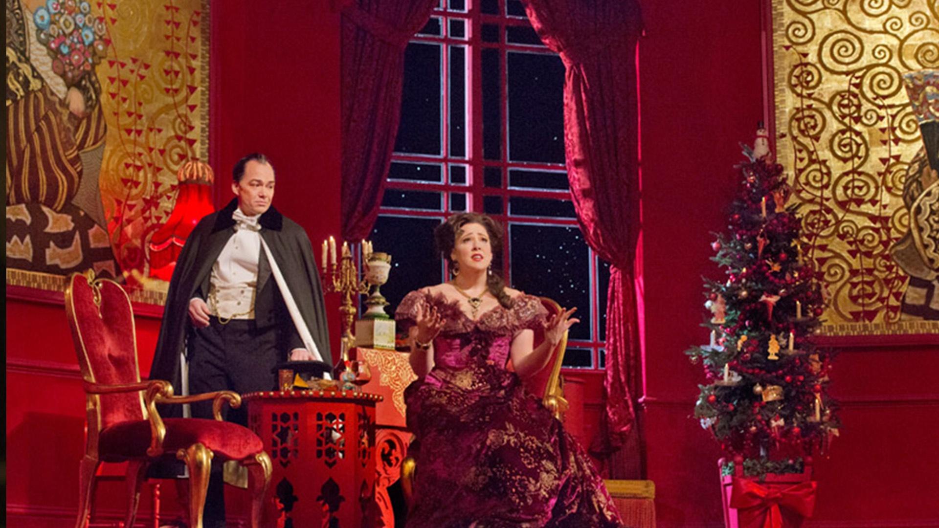 A scene from Die Fledermaus at the MET Opera with a Christmas tree and a man and woman in fancy clothing