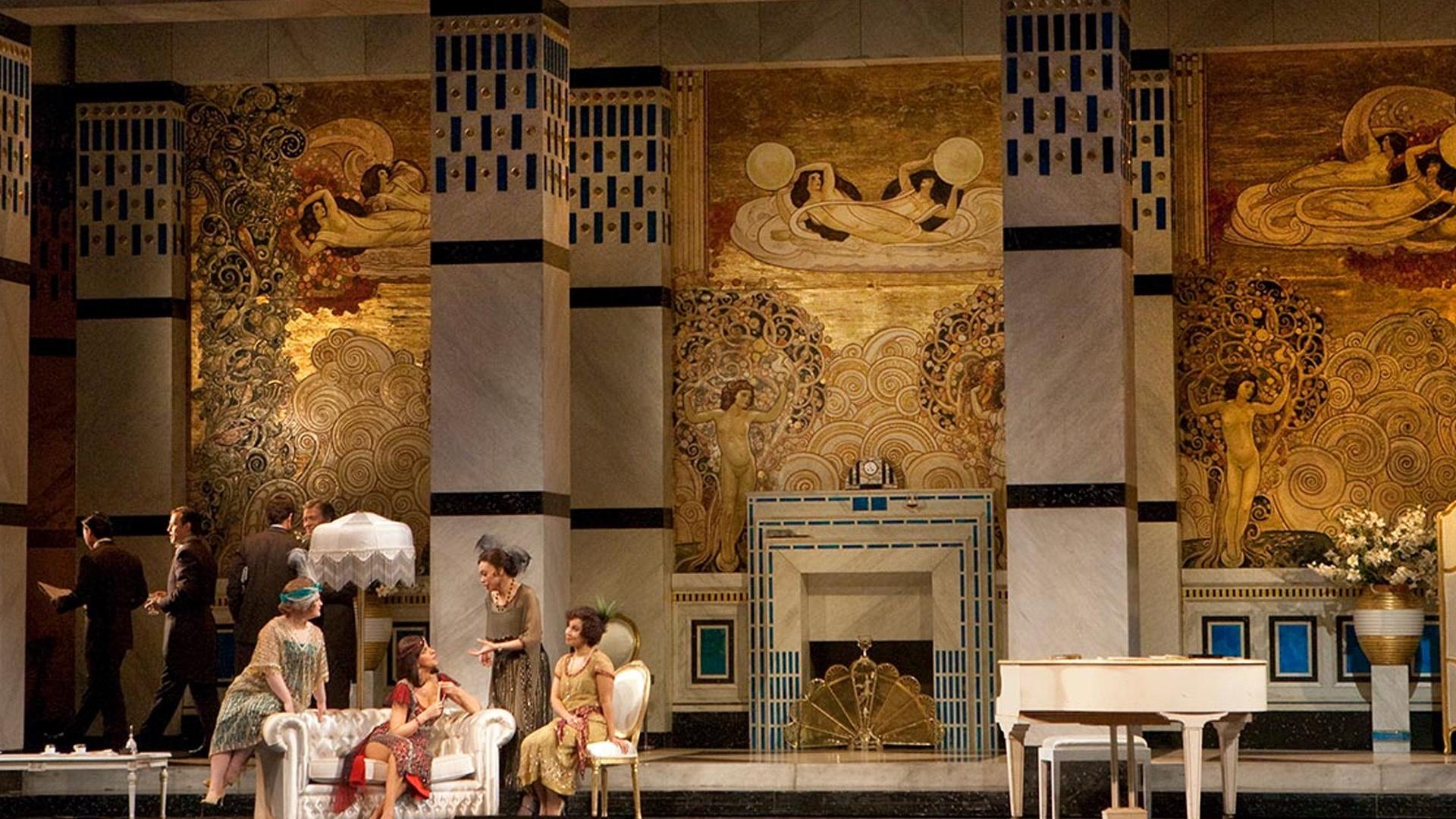 a scene from La Rondine where women, dressed in fancy clothing, are gathered together and conversing with one another