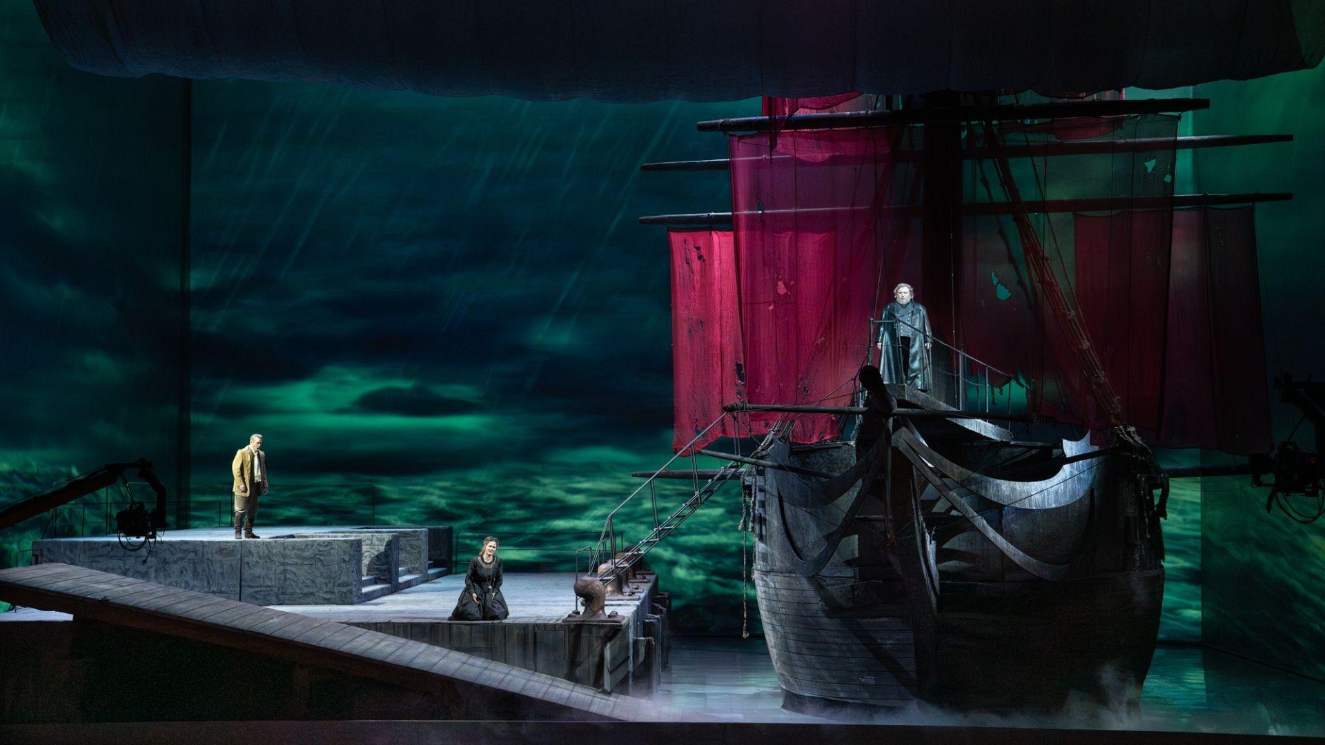 A scene from "Der fliegende Holländer", where the ship is docked and a man and woman stack on the dock, with another man at the bow of the ship