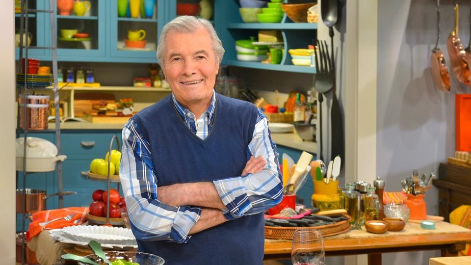 Jacques Pépin standing in a kitchen with his arms folded across his chest