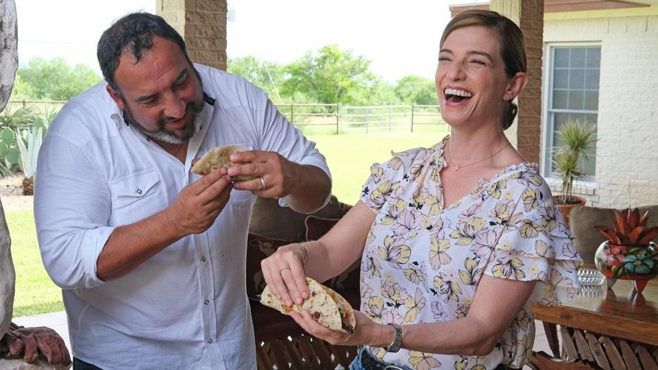 Pati Jinich and a man laughing and enjoying tacos