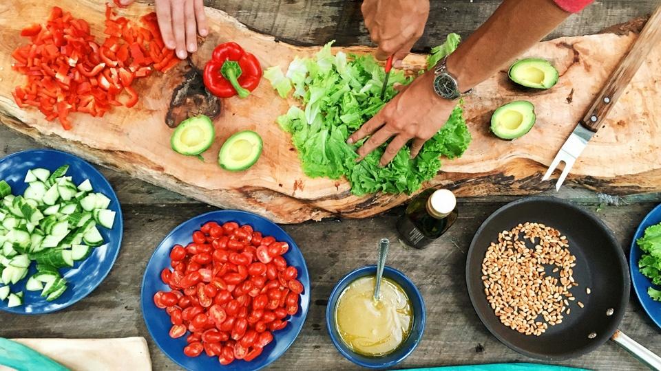 Hands chopping up various ingredients, including peppers and cucumbers