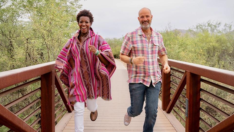 A woman and man happily running across a wooden pedestrian bridge