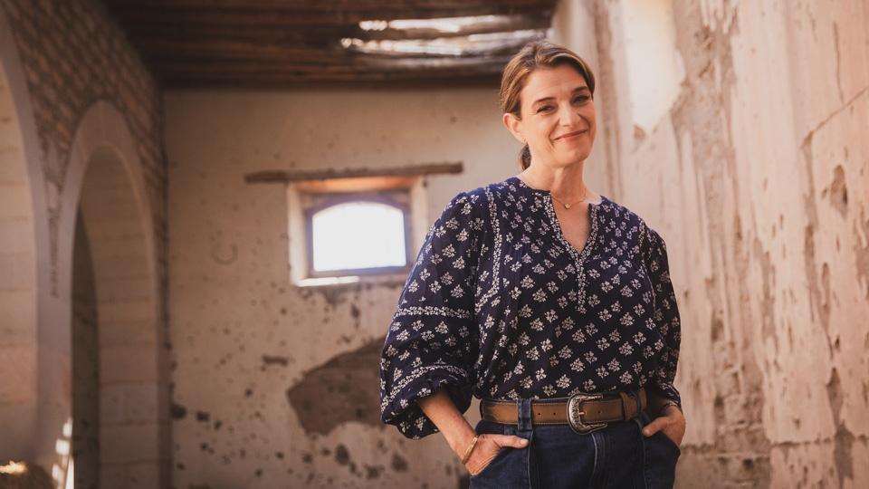 Pati Jinich soft smiling for a photo, standing with her hands in the front pockets of her jeans