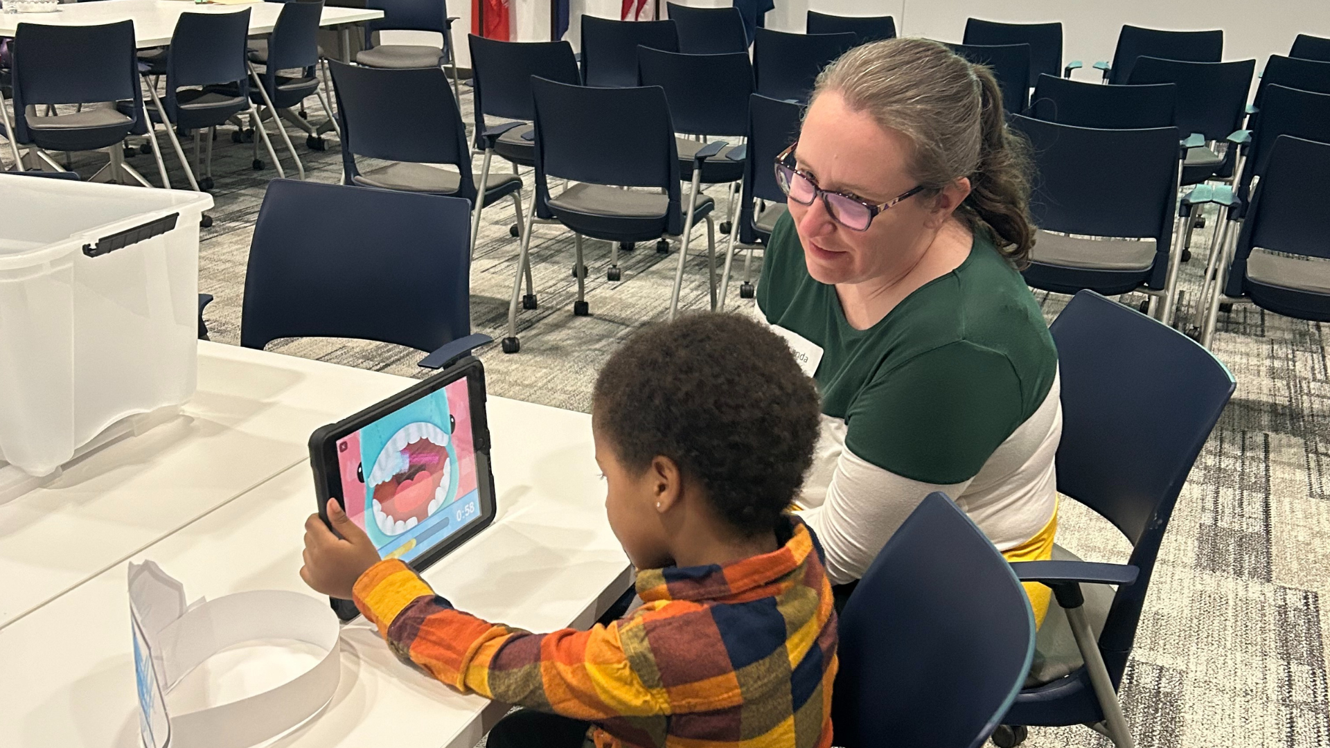 A n adult sitting with a child who is watching an educational video on a tablet