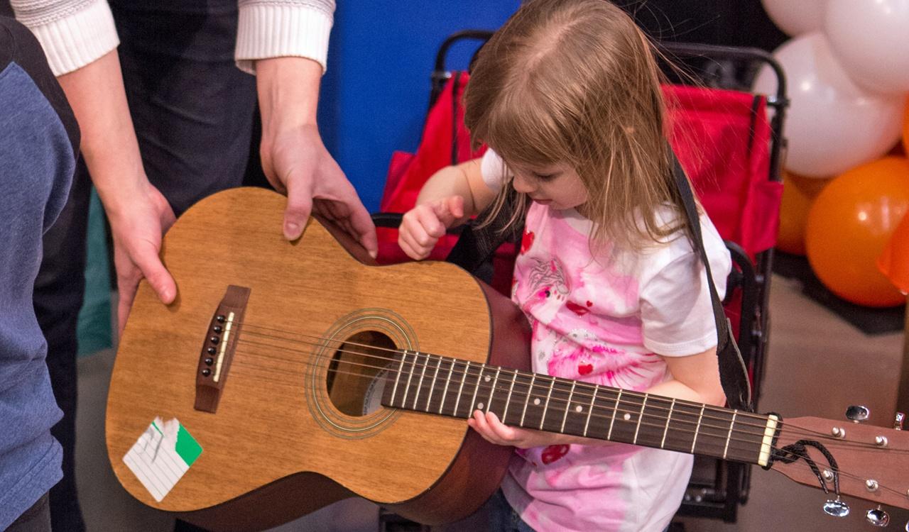 Young girl tries our the guitar with the help of the Community Music School