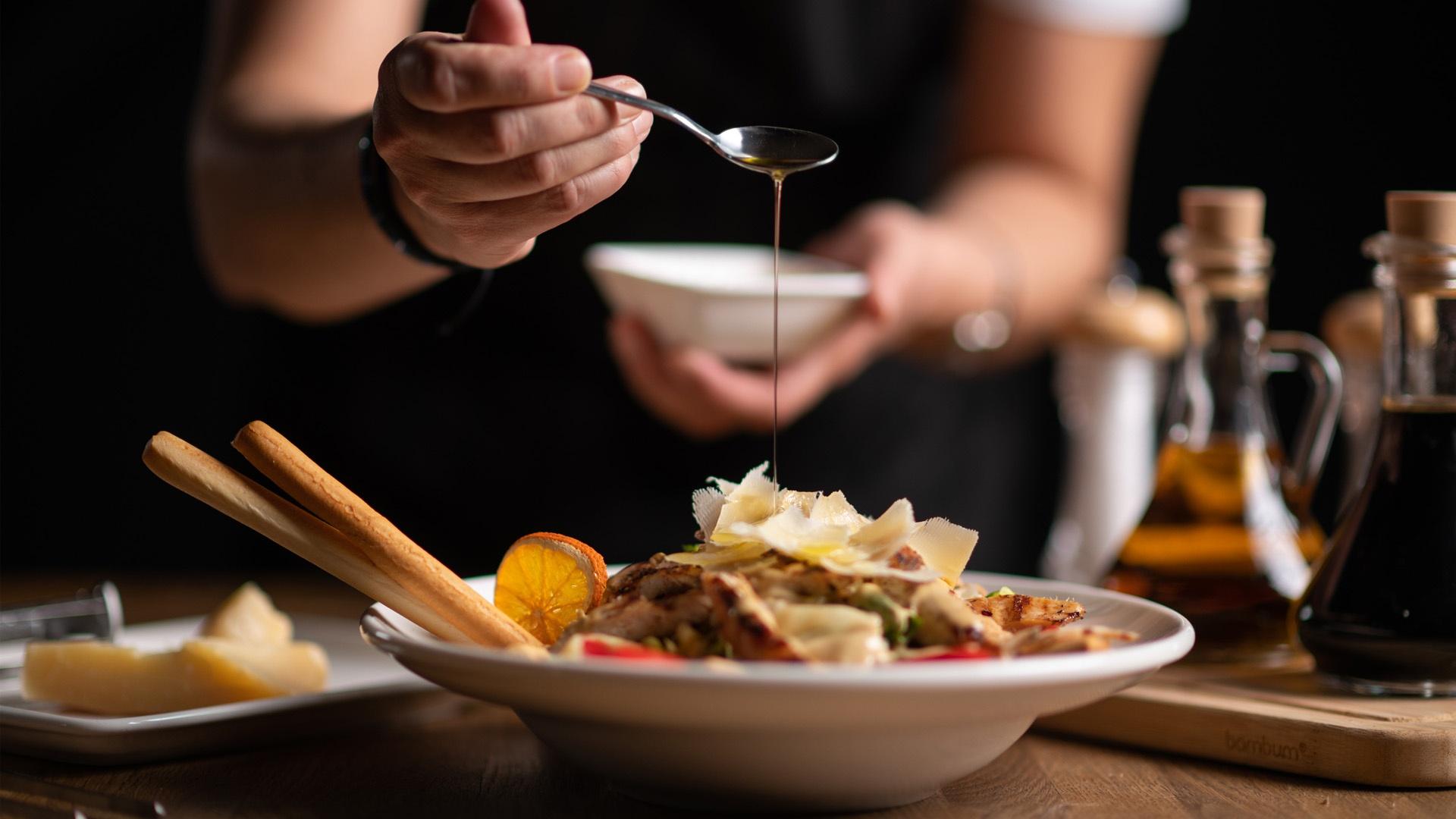 drizzling sauce over a dish of food