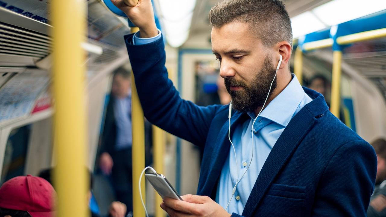 man with earbuds looking at phone while commuting to work