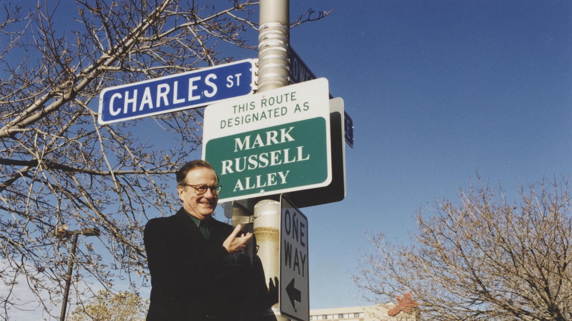Mark Russell in fron t of sign designating Charles St. in Buffalo as "Mark Russell Alley"