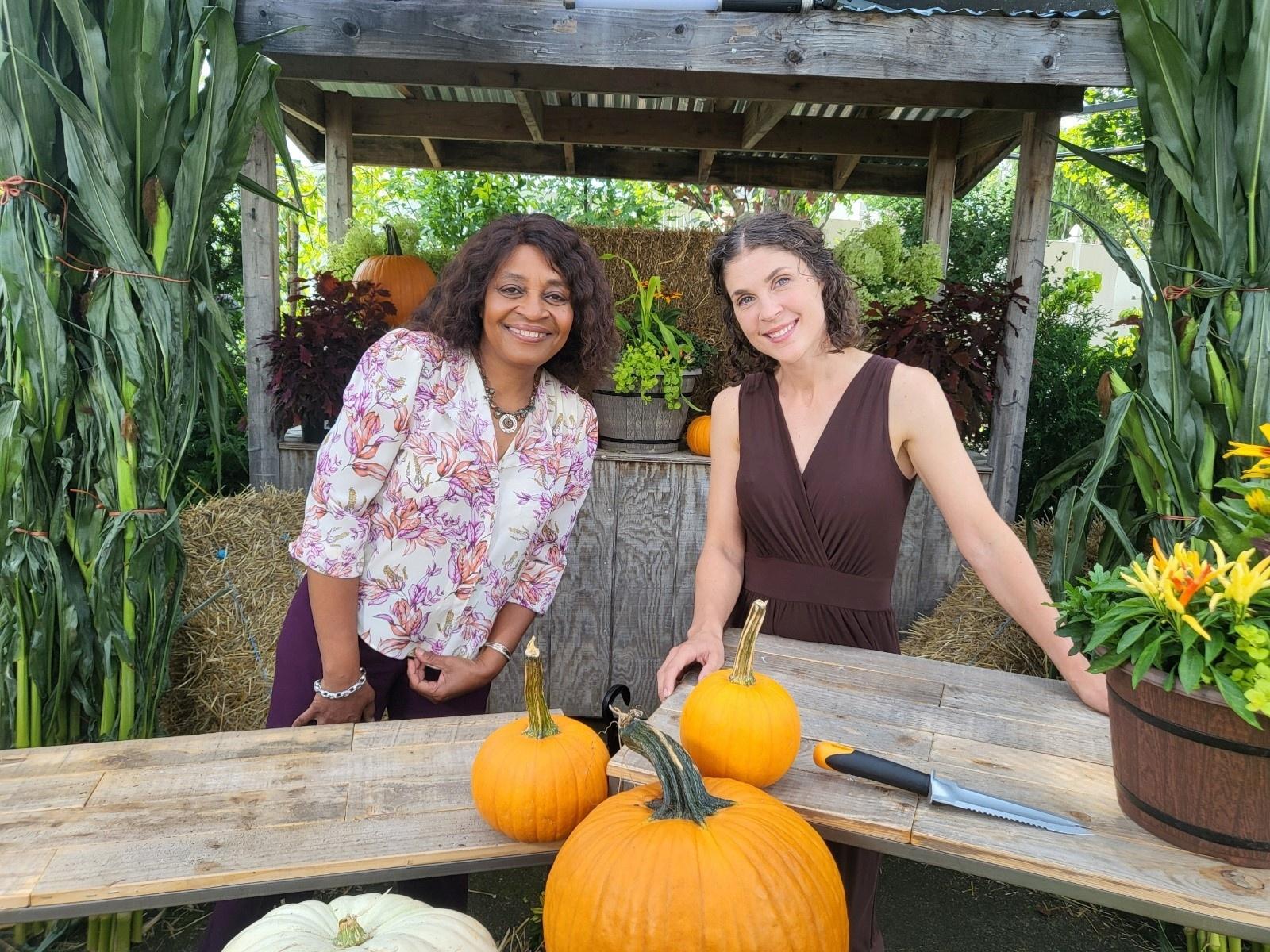 Hosts Nora Saintz and Sylvia Bennett smiling in front of tables with pumpkins on them