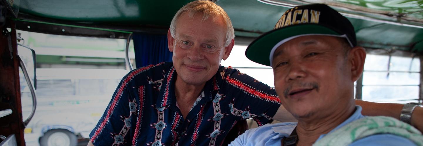 Martin Clunes and a Filipino man smiling at the camera while inside a bus.