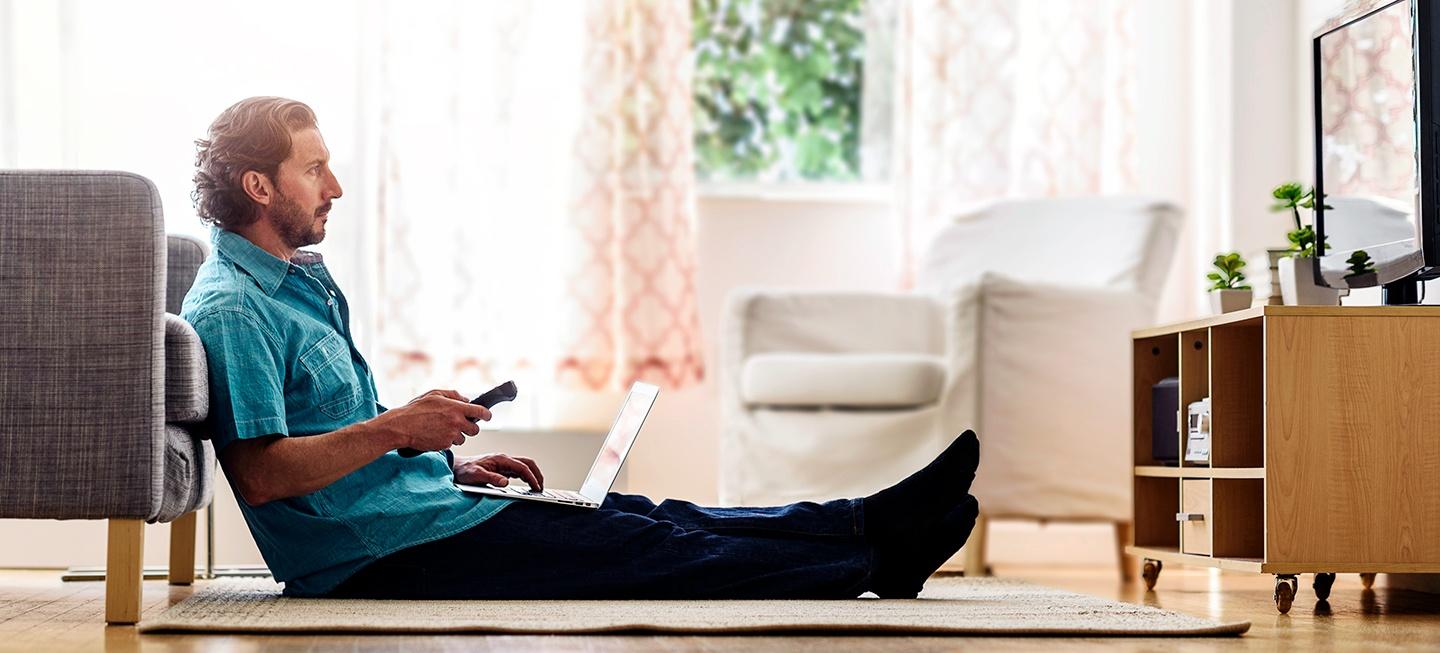 Man sitting on floor with laptop watching TV