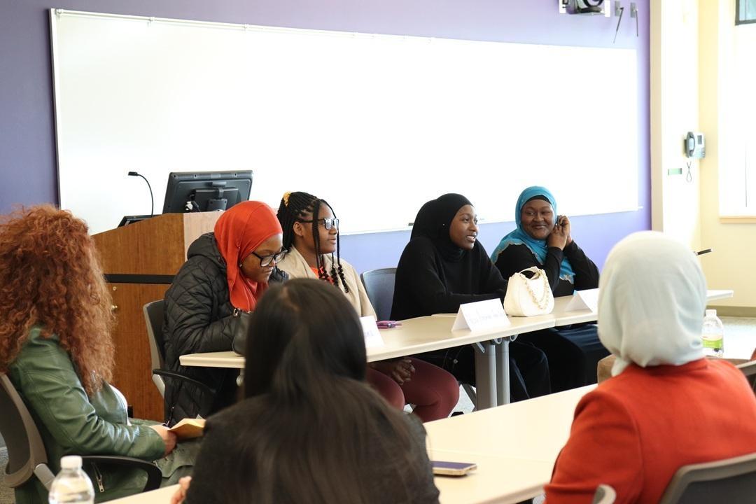 Students sit facing each other at long tables in a classroom