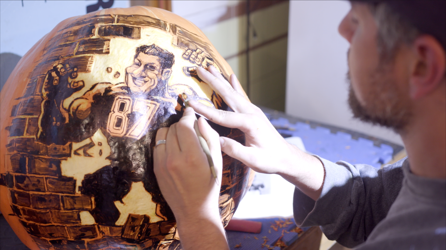 Artist carving a caricature of Rob Gronkowski, number 87, into a pumpkin.