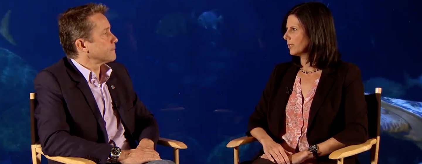 Fabien Cousteau, seated, speaking with Alison Lebovitz in front of a large tank at the Tennessee Aquarium