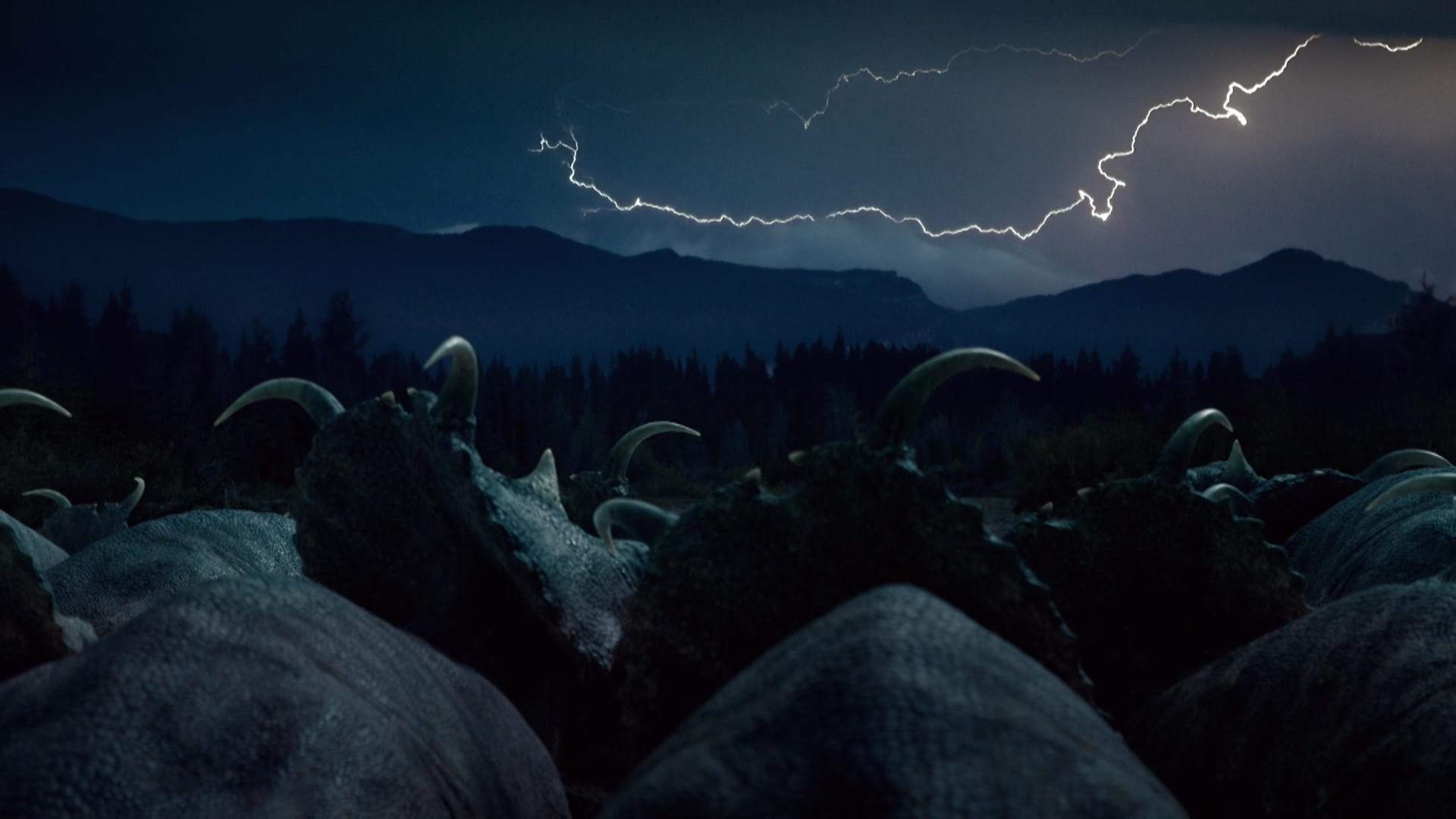 A herd of dinosaurs in the dark with lightening filled sky. 