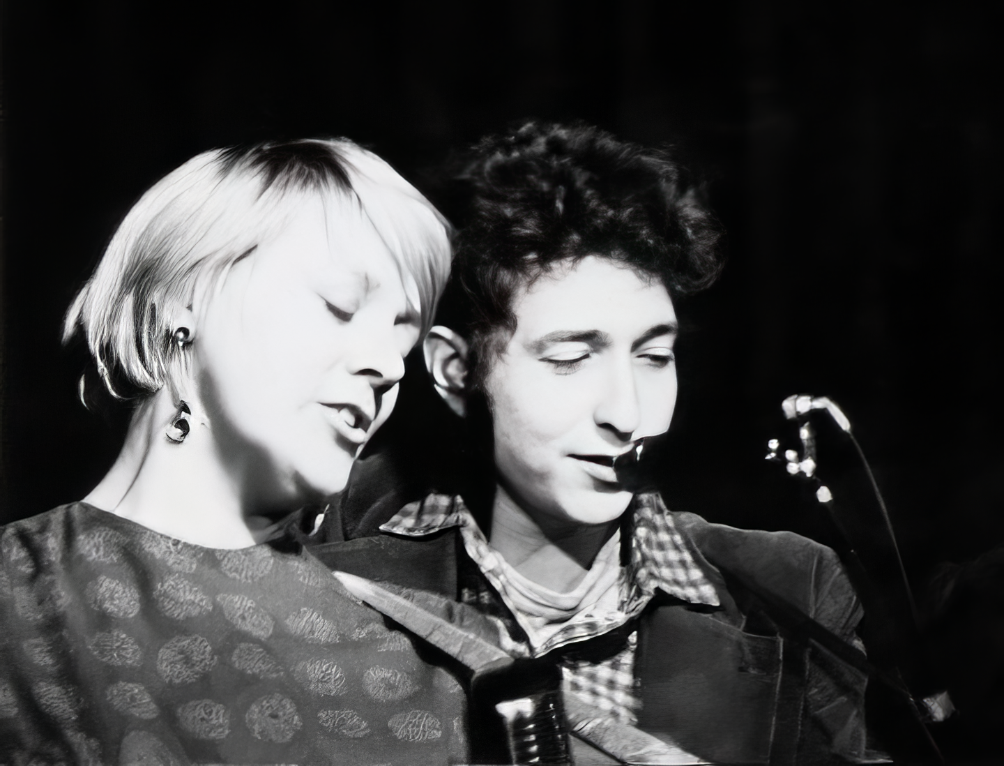 An old photo of Barbara Dane with Bob Dylan standing closely behind her as they sing into the microphone together