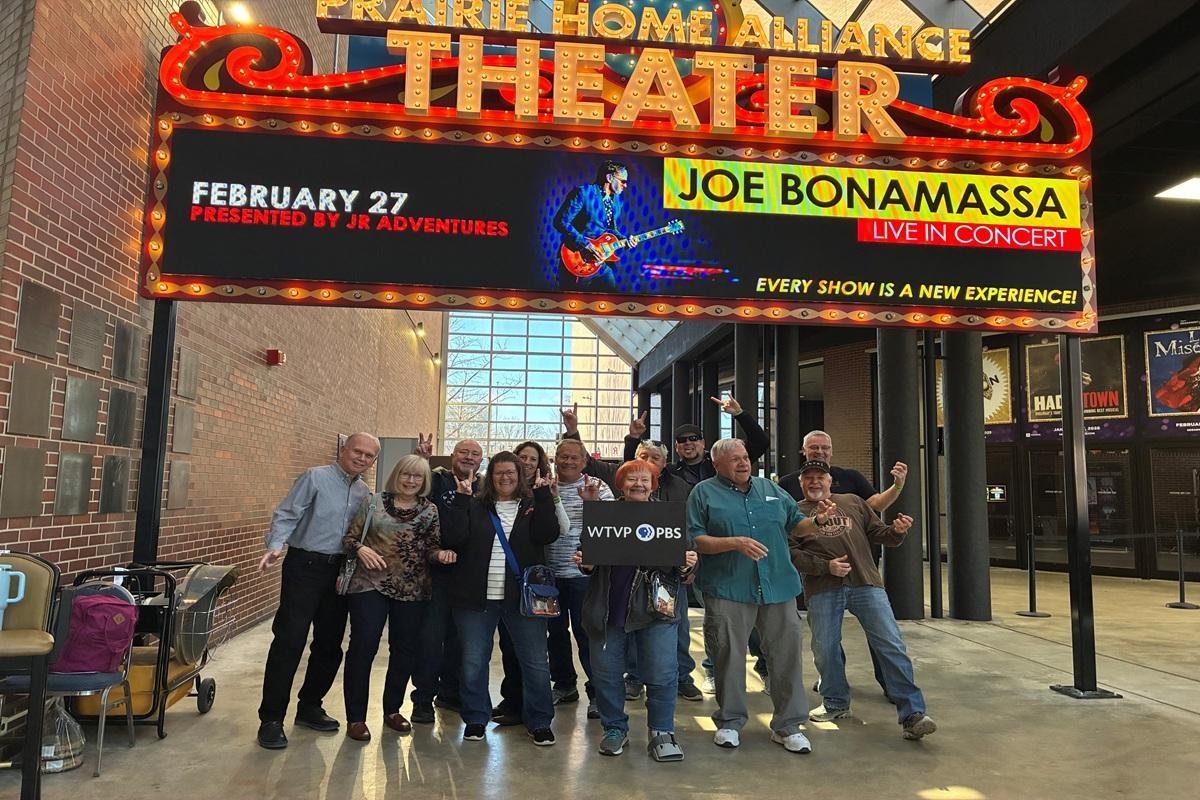 A dozen people stand under a Joe Bonamassa sign before a concert