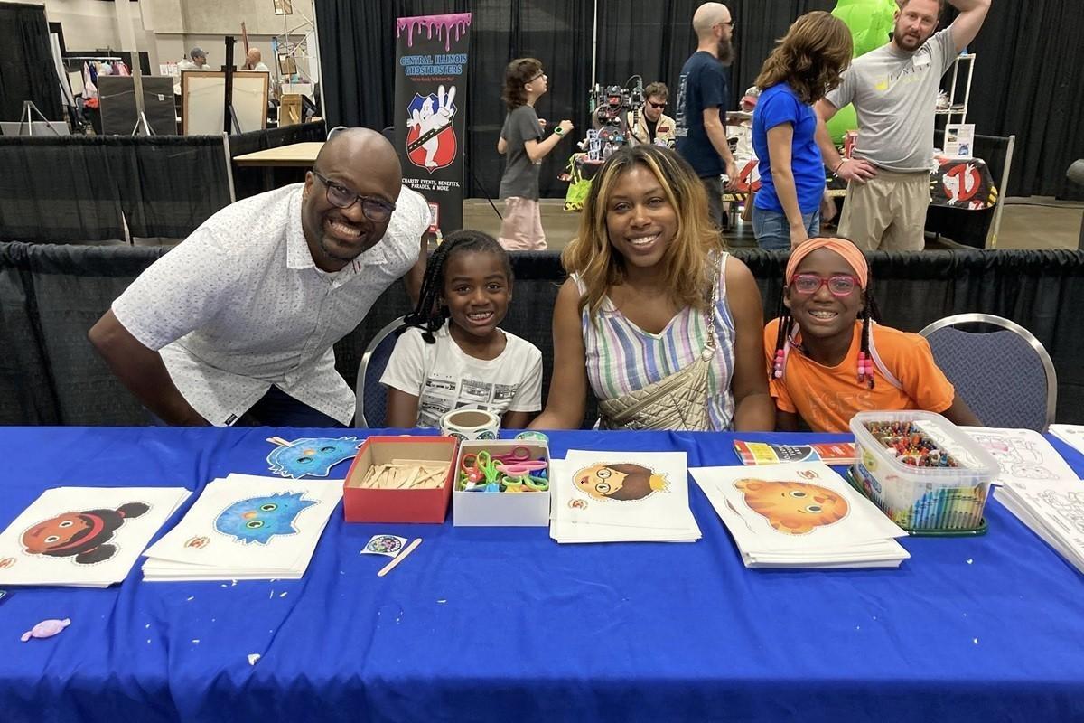 A family of four sits at a blue craft table at a WTVP event