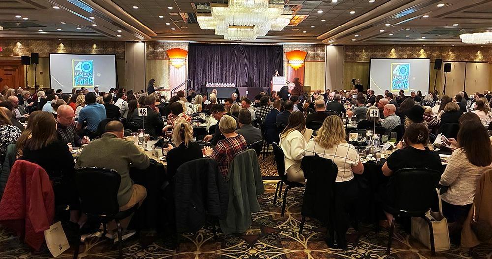 A wide shot of the award ceremony ballroom with people sitting at tables in the foreground, stage and video screens in the background