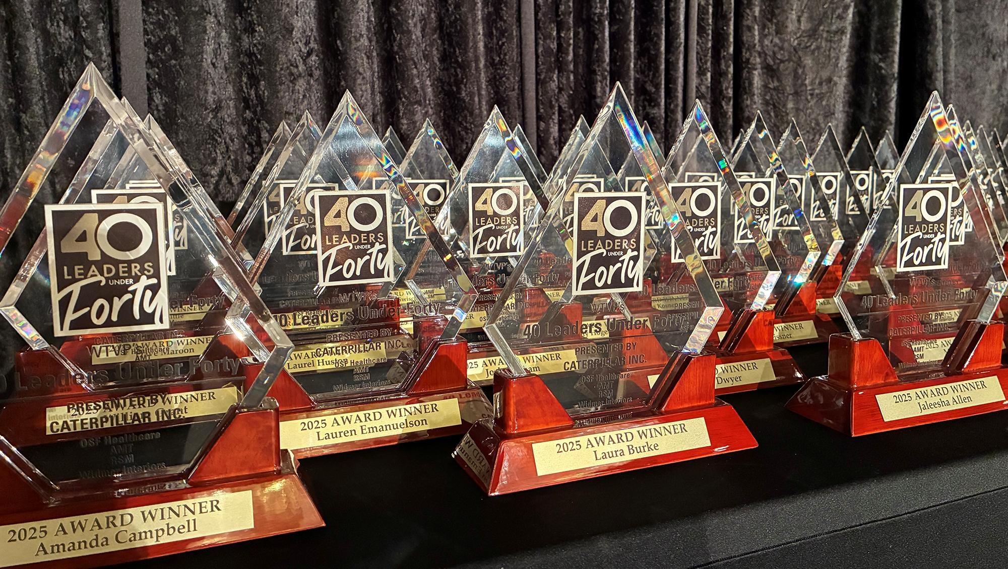 A group of 40 Leaders Under Forty Awards sitting on a table in front of black drapes