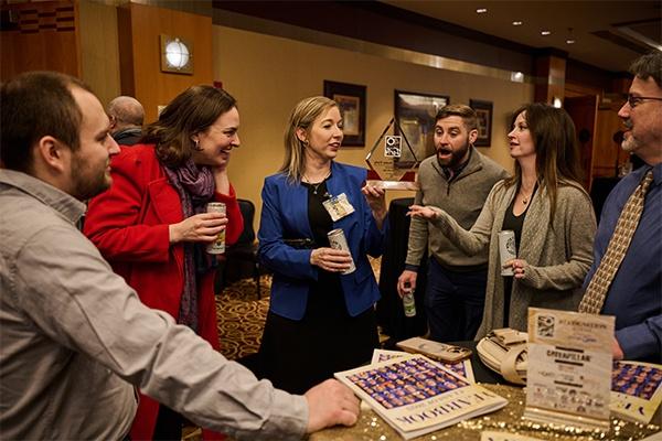 Class of 2025 member, Kaie Fitch holding her award with a group of people starting around a tall table.