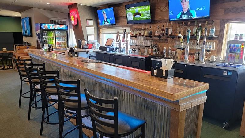 Wooden bar with high stools, beer taps, liquor bottles, and wall-mounted TVs showing golf.