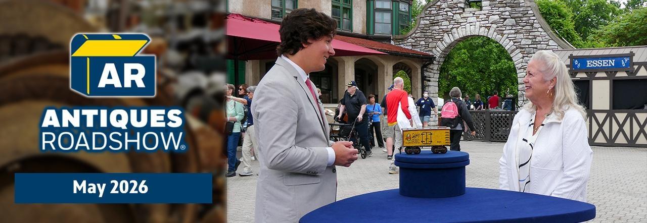 A man and woman discussing a toy train car, also includes the Antiques Roadshow logo with the text May 2026.