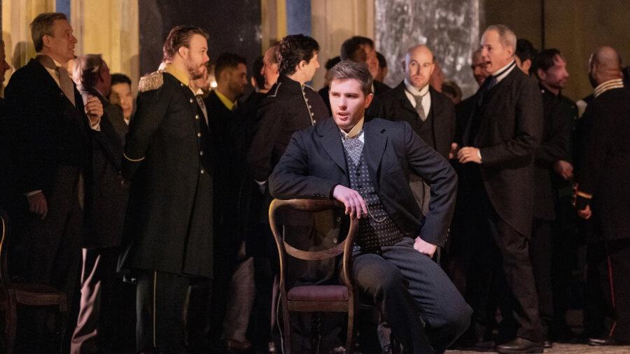 A young, bored, Eugene Onegin, portrayed by Igor Golovatenko, sits in formal attire in a ballroom full of other formally dressed men as the title character of Tchaikovsky's adaptation of Alexander Pushkin's original work.