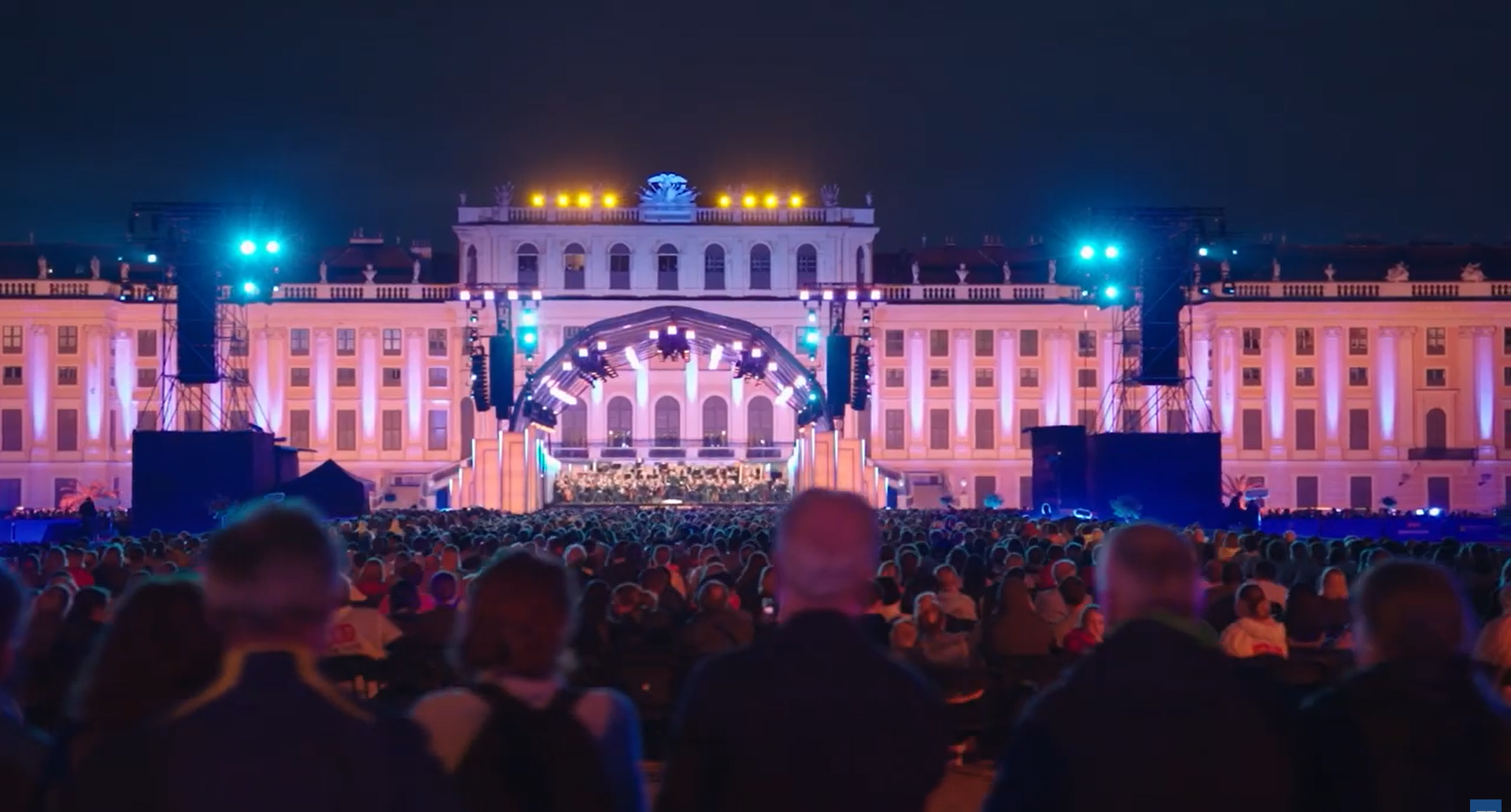 The Vienna Philharmonic Summer Night Concert for 2026 is depicted beyond a vast audience and setting before the brightly lit Schönbrunn Palace.