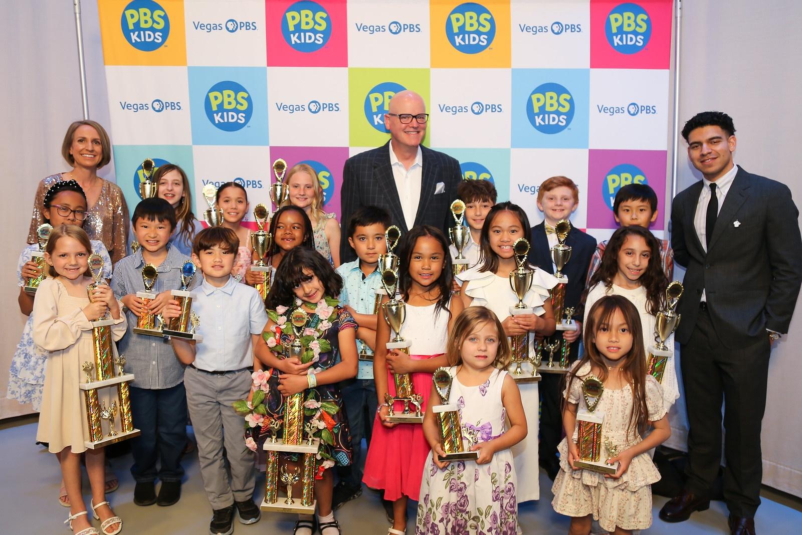 A group of children holding trophies standing against a PBS KIDS backdrop