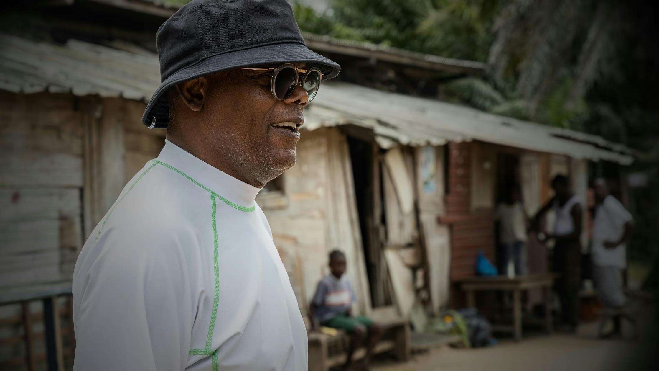 Samuel L. Jackson smiles as he wears sunglasses, a bucket hat, and a white shirt