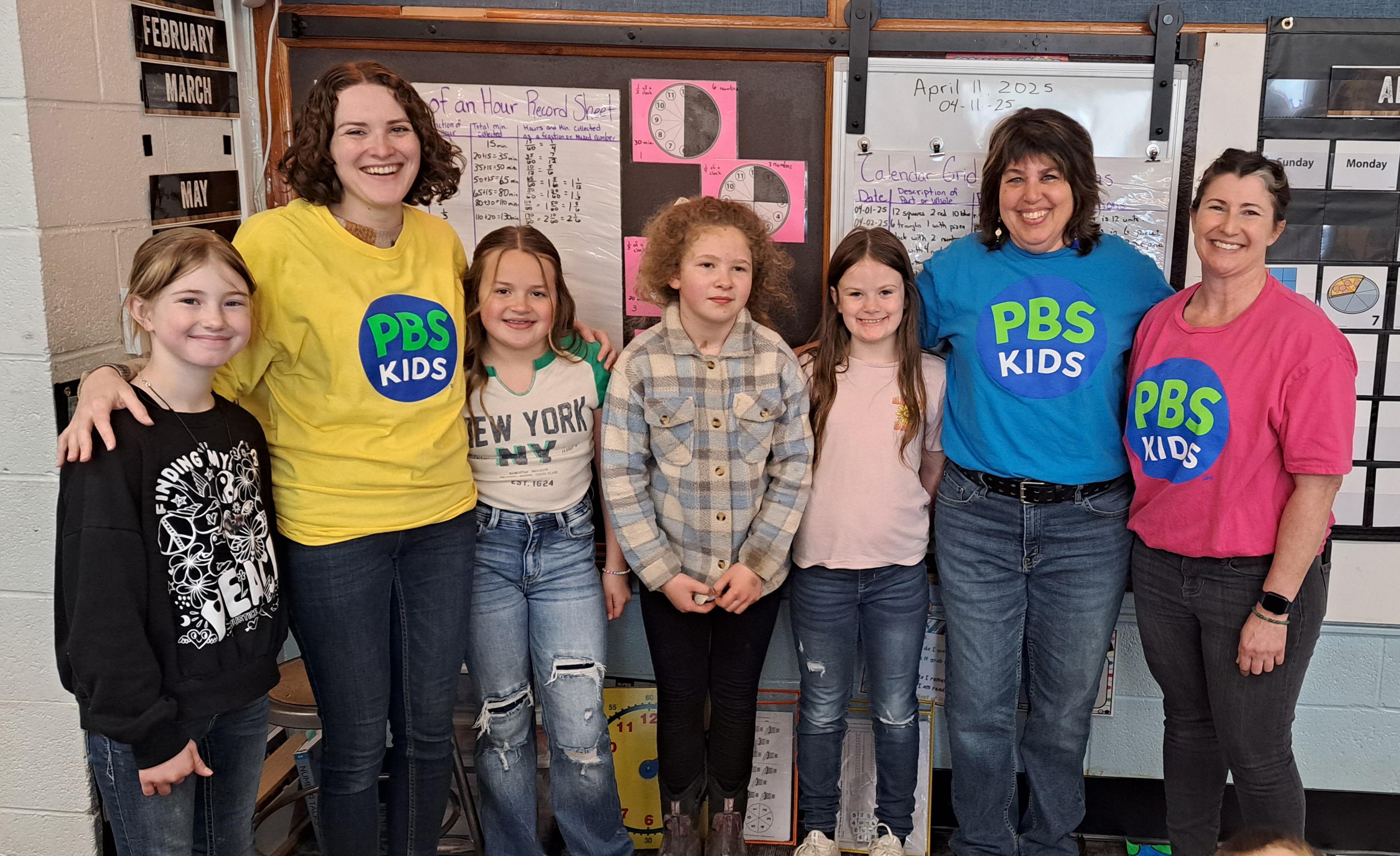 A group of young children are smiling at the camera with adults in PBS KIDS shirts