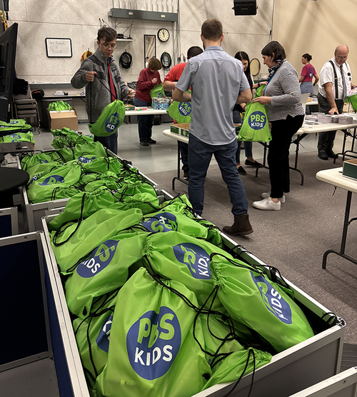 Volunteers pack green bags full of kindergarten kits