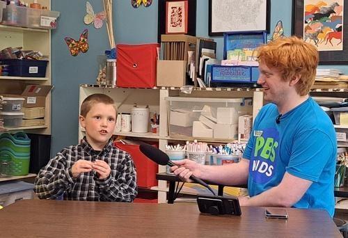 A young boy is talking to an IdahoPTV employee holding a microphone