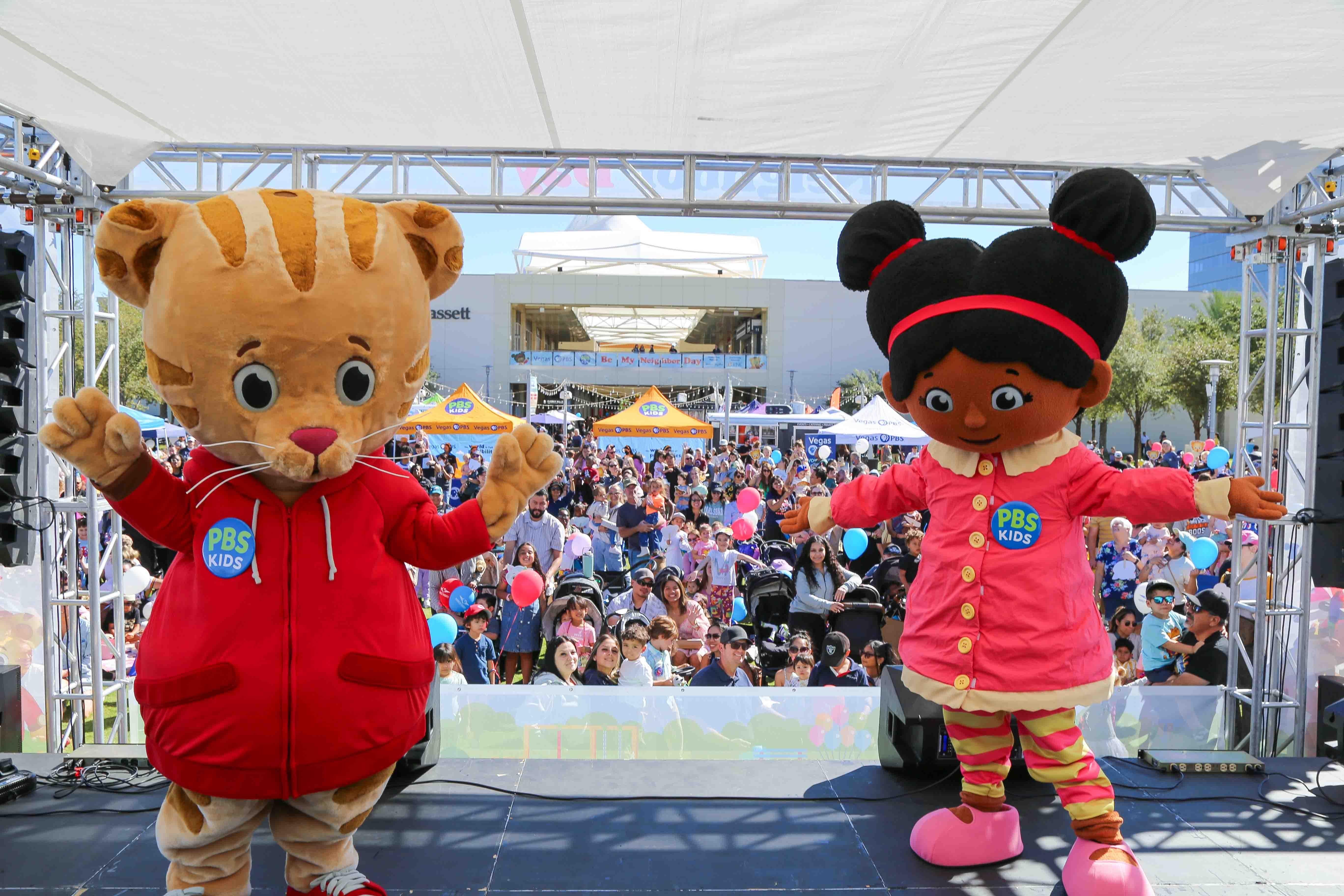 Daniel Tiger and Miss Elaina mascot characters standing on an outdoor stage