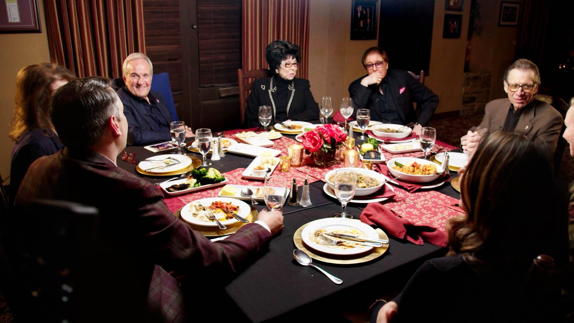 Camille Ruvo, Larry Ruvo, Lorraine Hunt-Bono, Dennis Bono, and Michael Severino sitting around a table at an Italian restaurant with various pasta dishes, water glasses, and empty wine glasses strewn about