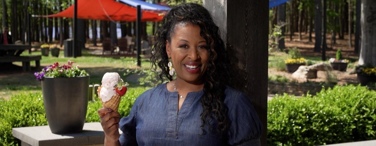 Host of NC Weekend, Deborah Holt Noel holding up an ice cream cone in front of a park.