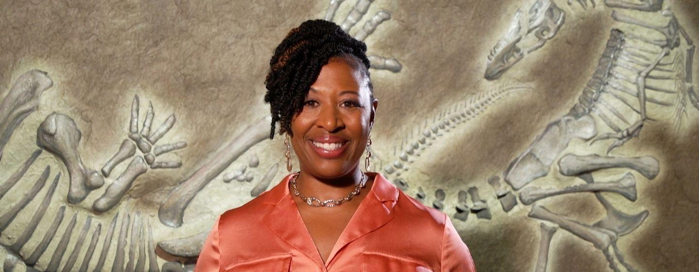 Deborah Holt Noel, host of NC Weekend in front of a dinosaur fossil mural.