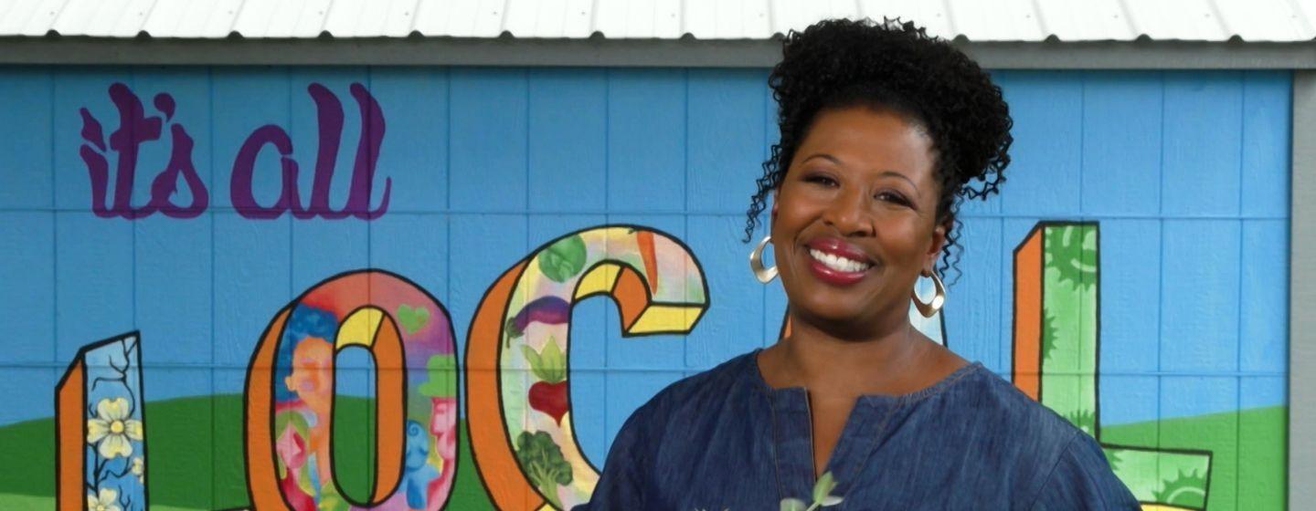 Deborah Holt Noel, host of NC Weekend in front of a mural that says, "It's all LOCAL."