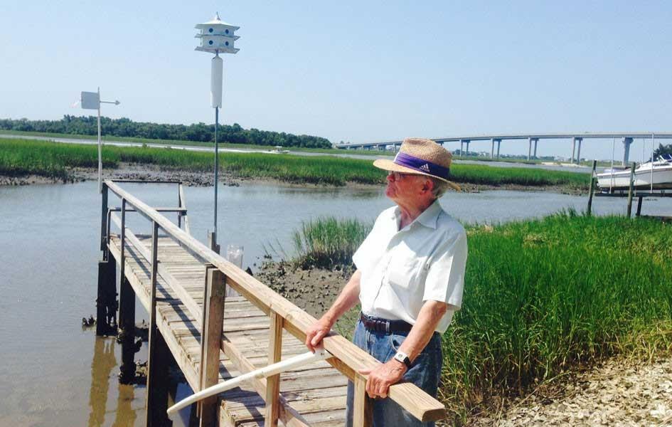 man standing on a small dock with sound and a large bridge in the background