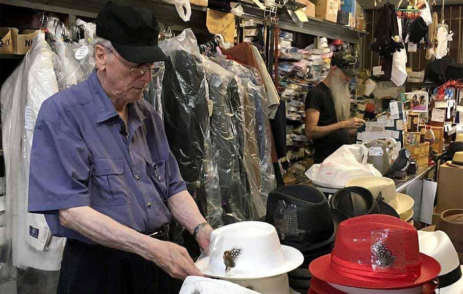 John Mitchell standing in store with hands on white hat with feather
