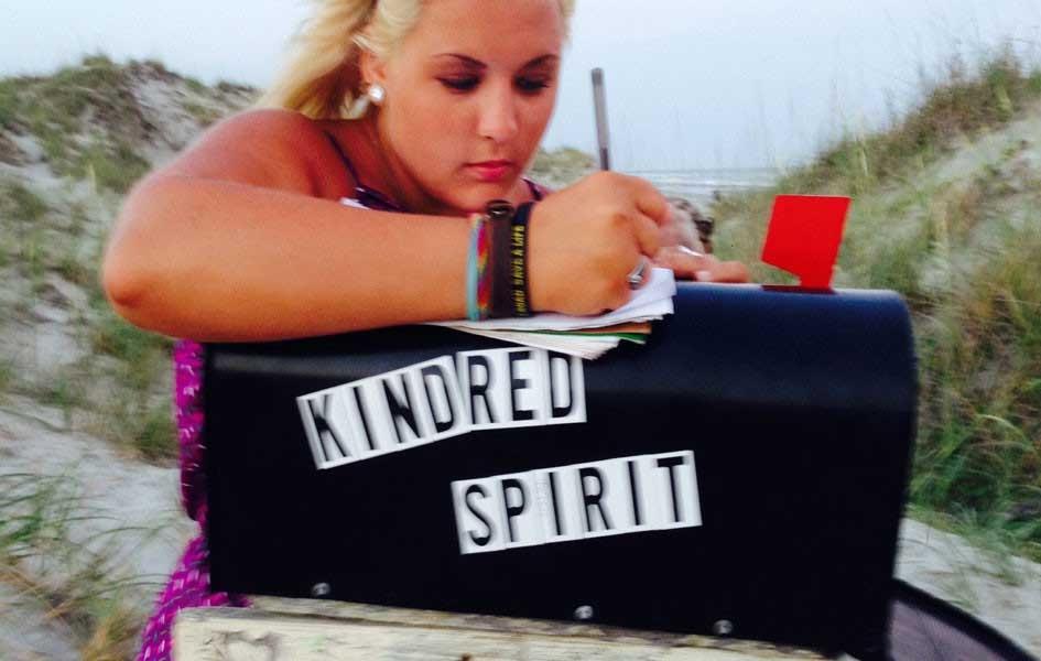 person writing letter on top of mailbox with words KINDRED SPIRIT on the side of it