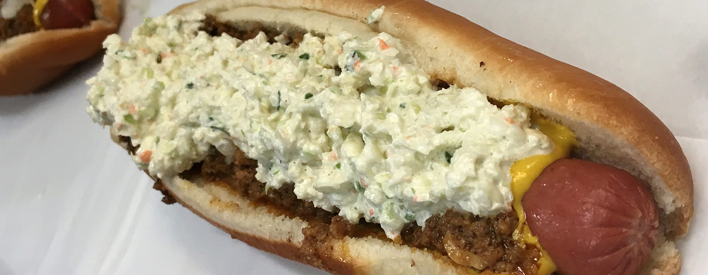 Hot dog in white bun placed on white background. Hot Dog is covered in slaw, and mustard