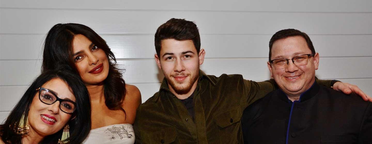 Denise Jonas, Priyanka Chopra, Nick Jonas, and Kevin Jonas Sr. stand with their arms around each other.