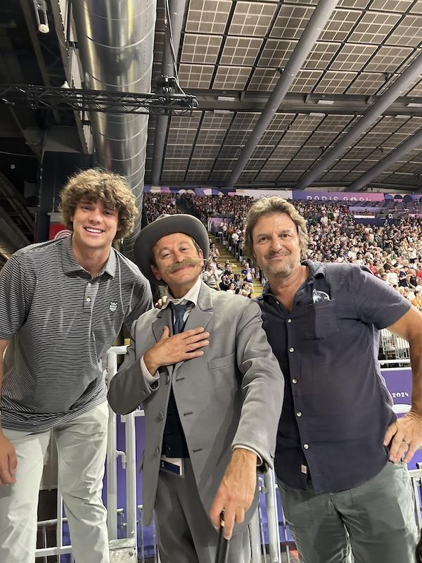 Three men pose with a seated crowd behind them.