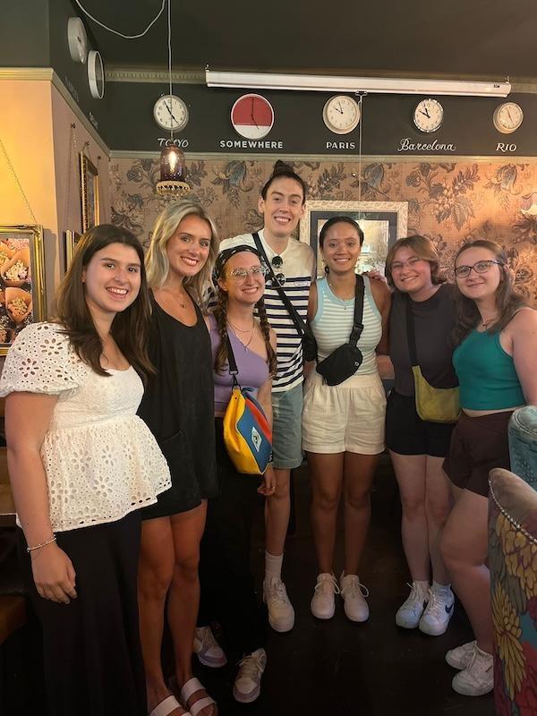 Six women pose in a semi-circle inside a London pub.