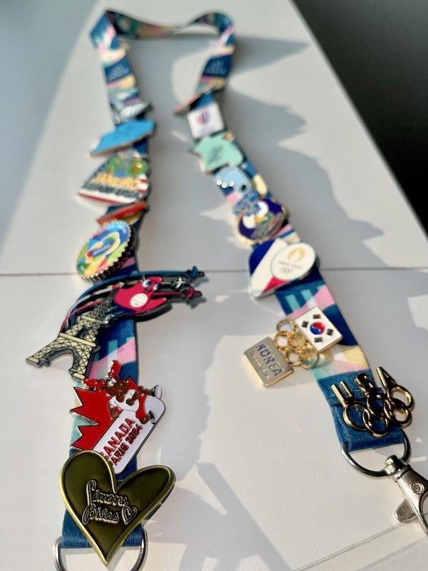 A lanyard covered in Olympics pins featuring previous Olympic games, and focused on the Simone Biles heart pin